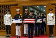Service members in uniform hold boxes draped in Korean and American flags.