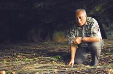 Chris Reyes, a World War II survivor, crouches in one of the caves where islanders, including his family, hid during the Japanese occupation of Guam.