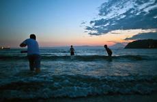 Children play in the water at Zushi Beach as the sun sets behind Mount Fuji.