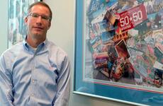 ESPN senior vice president Mark Gross stands by a commemorative collage from ESPN&#39;s 50 States in 50 Days summer series in 2005. The series included a stop at the 2005 All-Armed Forces Women&#39;s Softball Tournament at Petersen Air Force Base, Colo.
