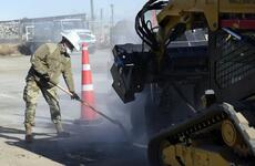 An airman uses a shovel to remove excess debris from the path of a wheel saw during a runway repair exercise at Yokota Air Base.