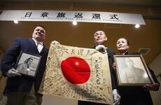 An American man poses with a signed Japanese flag held by a Japanese pair.