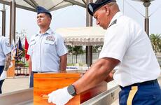 A soldier in dress uniform and white gloves places a wooden case into a casket, while another soldier in dress uniform stands at attention next to the casket.