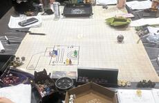 A Dungeons and Dragons playing board sits on a table surrounded by dice, paper and notebooks.