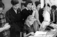 Miss Haruko Ota, a third grade teacher, peeks over the shoulder of Brenda Sheets, 10, daughter of Master Sgt. and Mrs. W. G. Sheets,