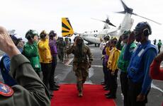 A U.S. Army general walks on a red carpet as a line of sailors salutes him aboard the USS Carl Vinson.