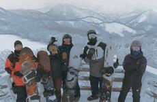 Five men holding snowboards pose for a picture in front of some mountains.