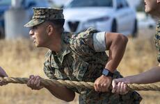 A Marine wearing a blouse with sleeves up tugs on a rope.