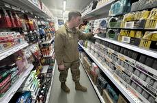 An airman in camouflage uniform looks at energy drinks on a store shelf.