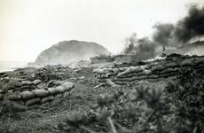 Military vehicles burn on an island during World War II.