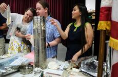 Three adults look at items in plastic bags that were put into a silver tube time capsule when they were children.