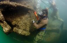Two divers in scuba gear survey the wreckage of a ship under water.