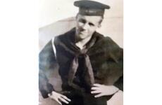 A black-and-white, 1940s-era portrait of a Navy sailor in hat and uniform posing with his hands on his hips.