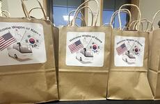 Brown paper grocery bags with white signs reading “Welcome Wagon of Korea” and pictures of U.S. and South Korean flags rest on a table.