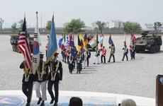 Service members carry member nation flags during a ceremony.