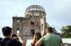 People take photos and read signs in front of the bombed wreckage of a domed building.