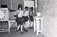 Three shirtless men wearing shorts and face masks are walking through a doorway.
