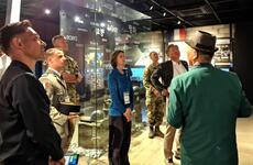 Julie MacKnyght looks at framed photos of an exhibition, surrounded by a professor and uniformed service members.