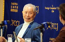 George Takei speaks to reporters in front of a blue backdrop.
