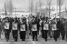 A black and white photo of people, mostly men in suits, walking while holding photos of Martin Luther King Jr.