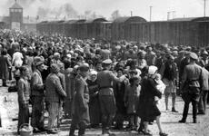 A black-and-white, 1940s-era photo of a large crowd of people standing next to a train at a station depot outside a World War II concentration camp.