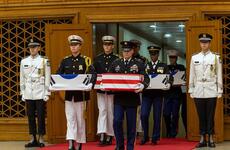 Service members in uniform hold boxes draped in Korean and American flags.