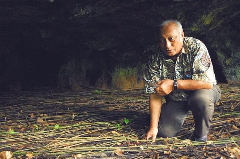 Chris Reyes, a World War II survivor, crouches in one of the caves where islanders, including his family, hid during the Japanese occupation of Guam.