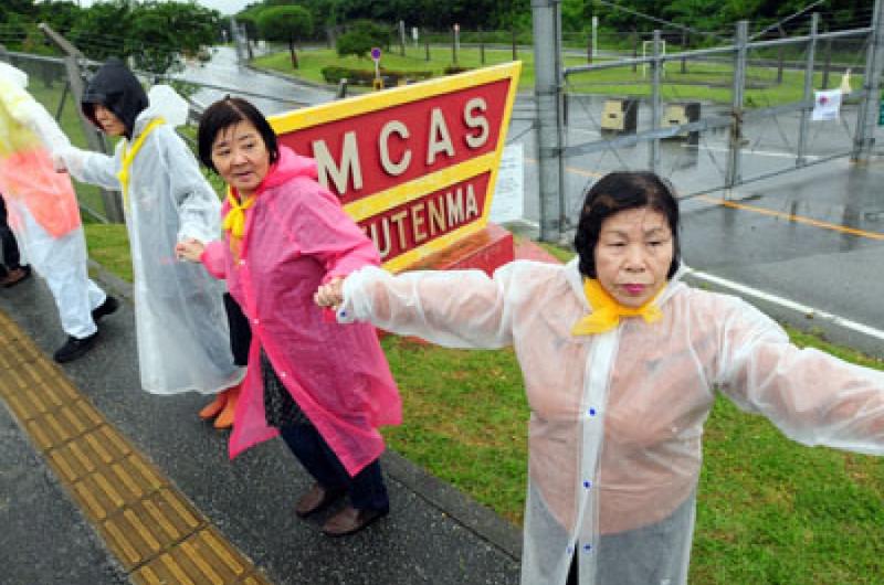 A few of the thousands of anti-base protesters at Marine Corps Air Station Futenma hold hands Sunday in front of the base sign.