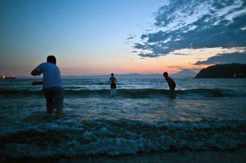 Children play in the water at Zushi Beach as the sun sets behind Mount Fuji.