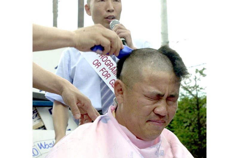 Lim Jong-han, a property owner, winces as other demonstrators protesting a new Army housing program shave his head Tuesday outside the gates of Yongsan Garrison.