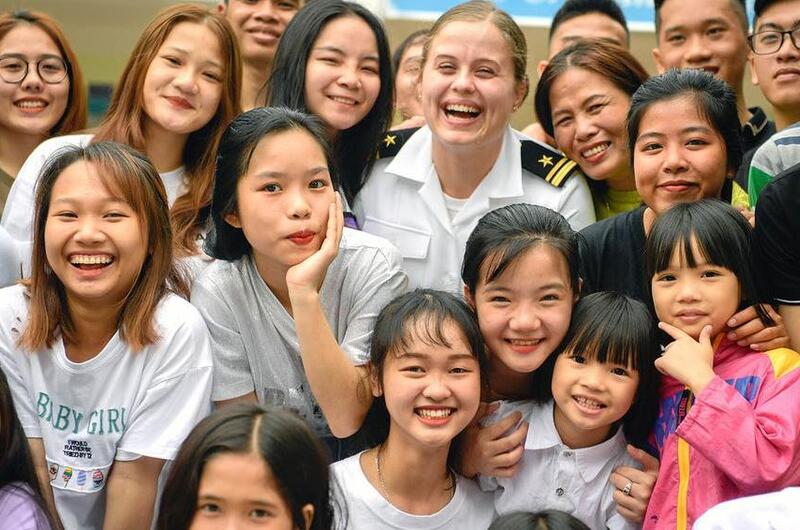 A Navy public affairs officer poses for a photo with children at the Dorothea's Project Legacies Charity Center, Danang, Vietnam, during the USS Theodore Roosevelt's port call March 6, 2020.