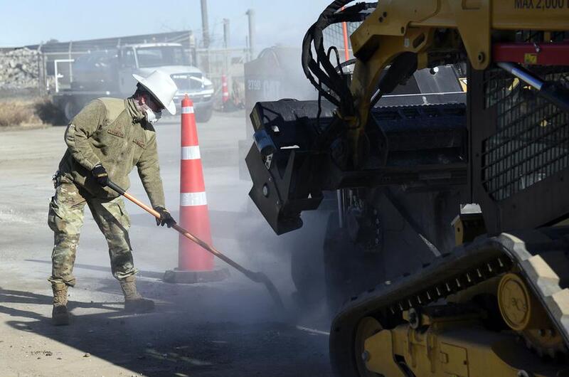 An airman uses a shovel to remove excess debris from the path of a wheel saw during a runway repair exercise at Yokota Air Base.