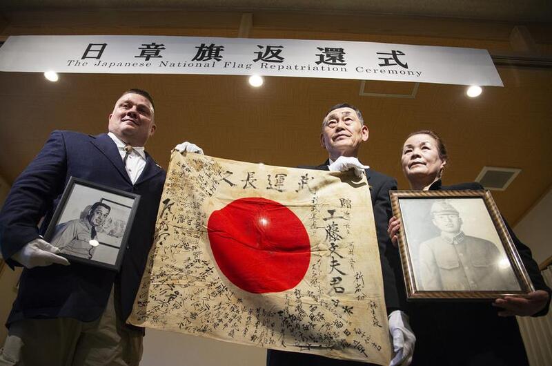 An American man poses with a signed Japanese flag held by a Japanese pair.