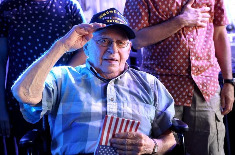 World War II veteran Arthur Grabiner salutes while holding an American flag.