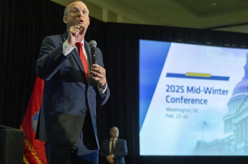 Collins stands with a microphone in his hand addressing the crowd.