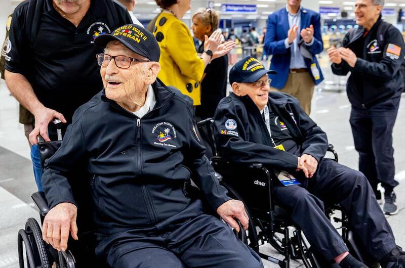 Two military veterans in wheelchairs are greeted at the airport.