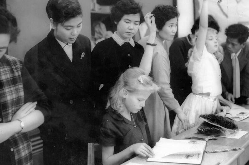 Miss Haruko Ota, a third grade teacher, peeks over the shoulder of Brenda Sheets, 10, daughter of Master Sgt. and Mrs. W. G. Sheets,