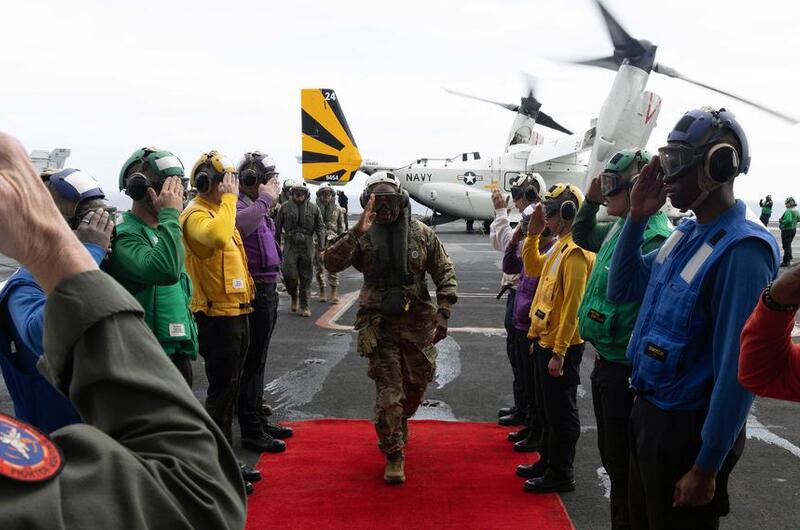 A U.S. Army general walks on a red carpet as a line of sailors salutes him aboard the USS Carl Vinson.
