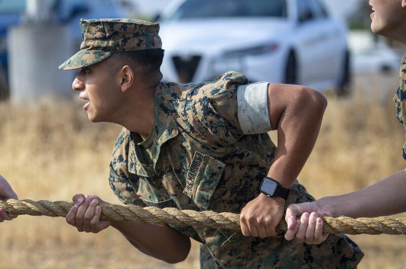 A Marine wearing a blouse with sleeves up tugs on a rope.