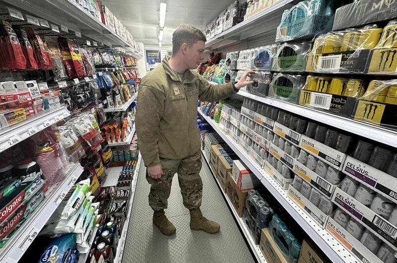 An airman in camouflage uniform looks at energy drinks on a store shelf.
