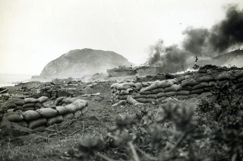 Military vehicles burn on an island during World War II.