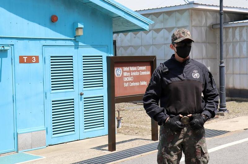A South Korean soldier stands guard in front of a blue building at the DMZ.