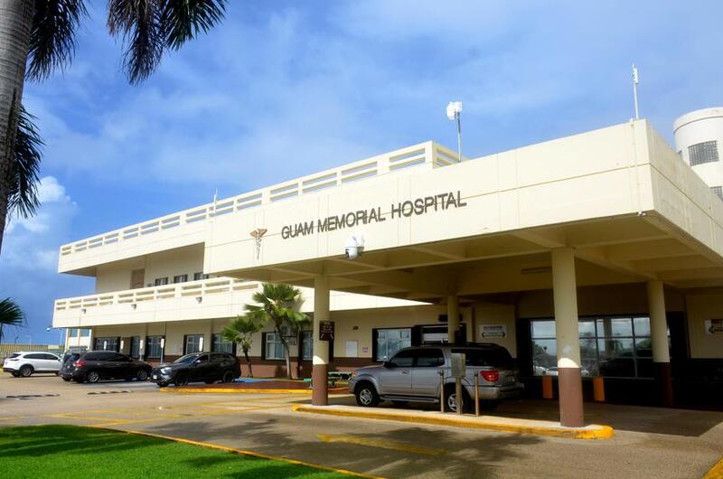 Cars are parked outside the front entrance of Guam Memorial Hospital in Tamuning, Guam, on a sunny day.