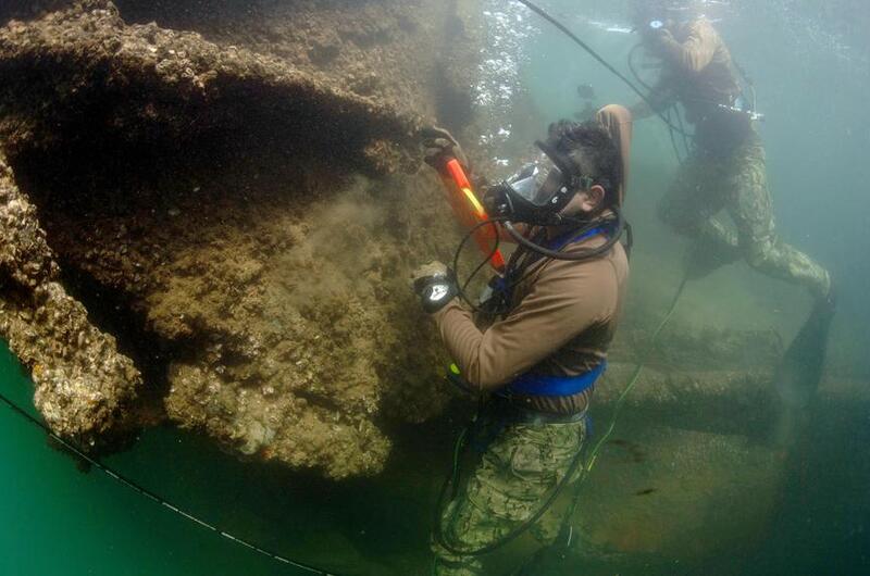 Two divers in scuba gear survey the wreckage of a ship under water.