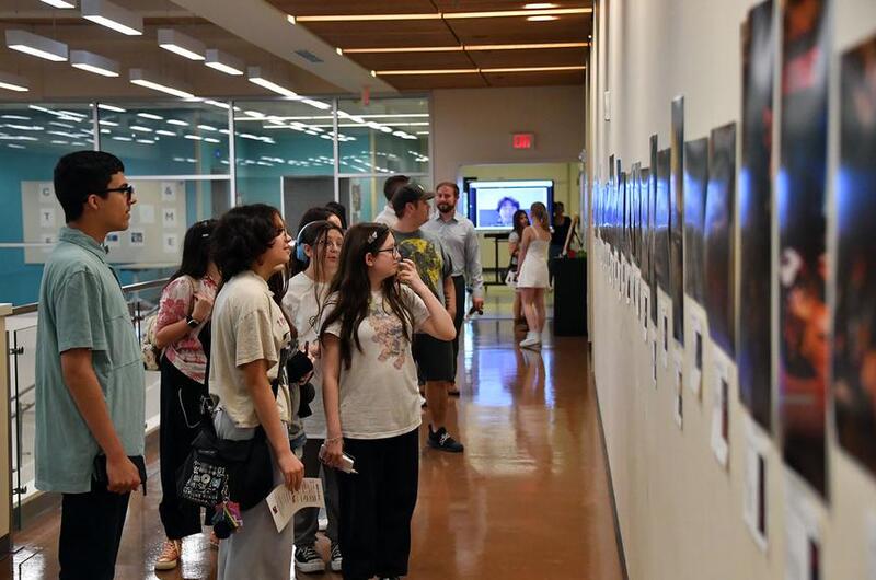 Students and visitors look at photographs on display.