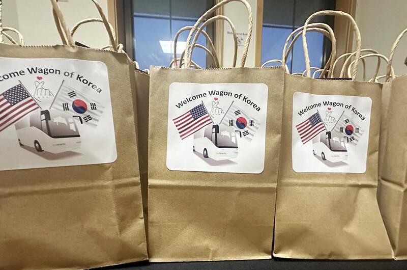 Brown paper grocery bags with white signs reading “Welcome Wagon of Korea” and pictures of U.S. and South Korean flags rest on a table.