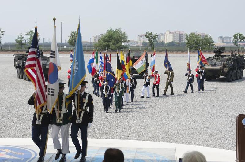 Service members carry member nation flags during a ceremony.