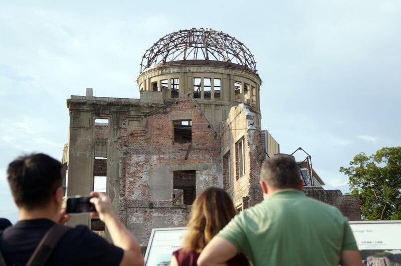 People take photos and read signs in front of the bombed wreckage of a domed building.