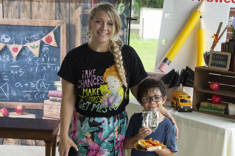 A mom and her son pose for a photo in front of school-themed props in a photo booth.