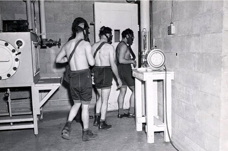 Three shirtless men wearing shorts and face masks are walking through a doorway.